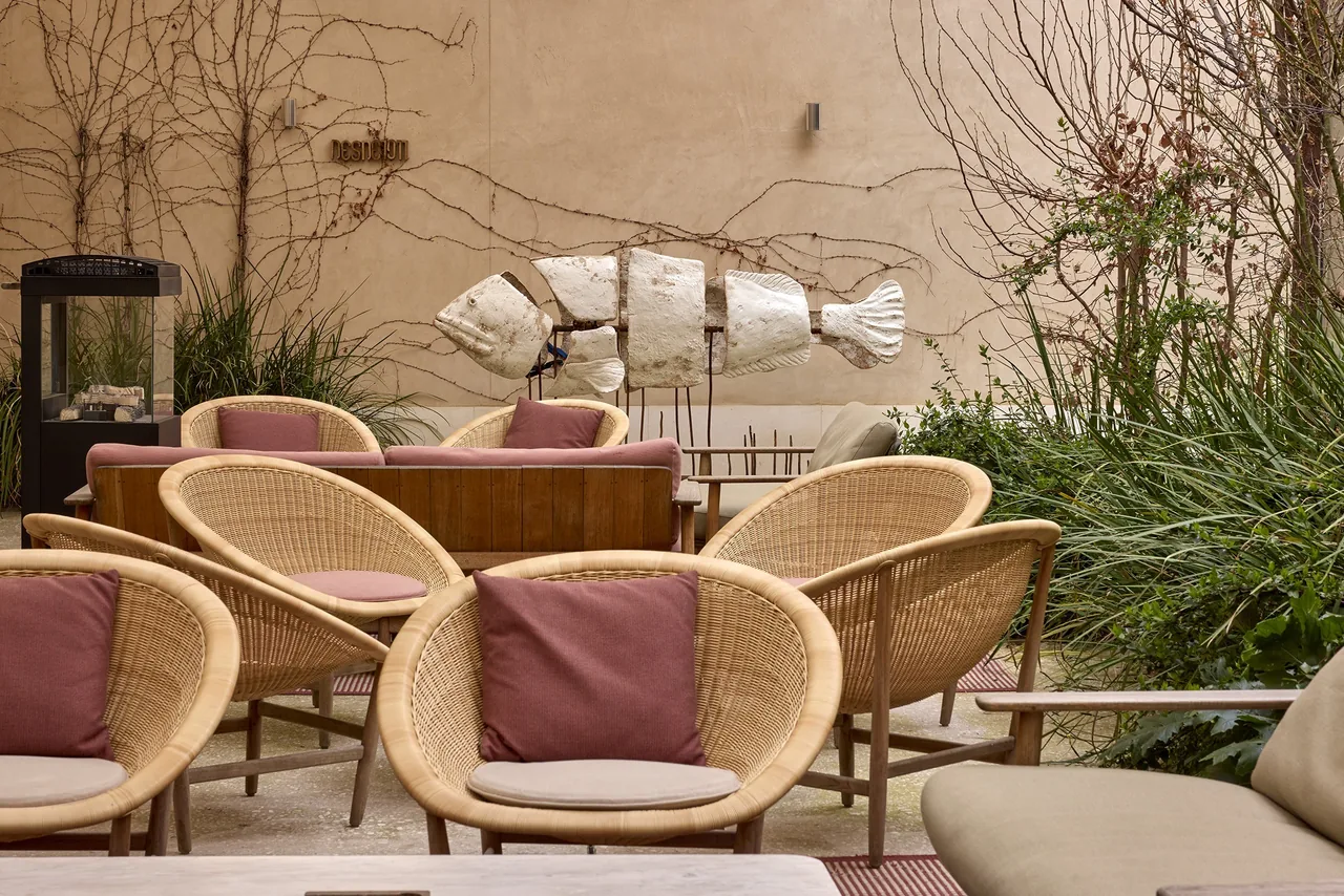 Wicker armchairs with cushions in a walled garden terrace with a fish sculpture and climbing plants