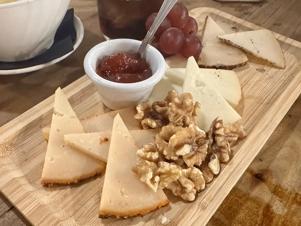 Wooden board with wedges of Spanish cheese, walnuts, red grapes and a ramekin of quince jam