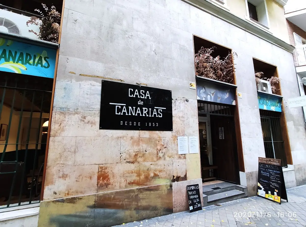 Street storefront with a black sign reading Casa de Canarias Desde 1953 and Detenderete branding on the awnings and an A-frame board