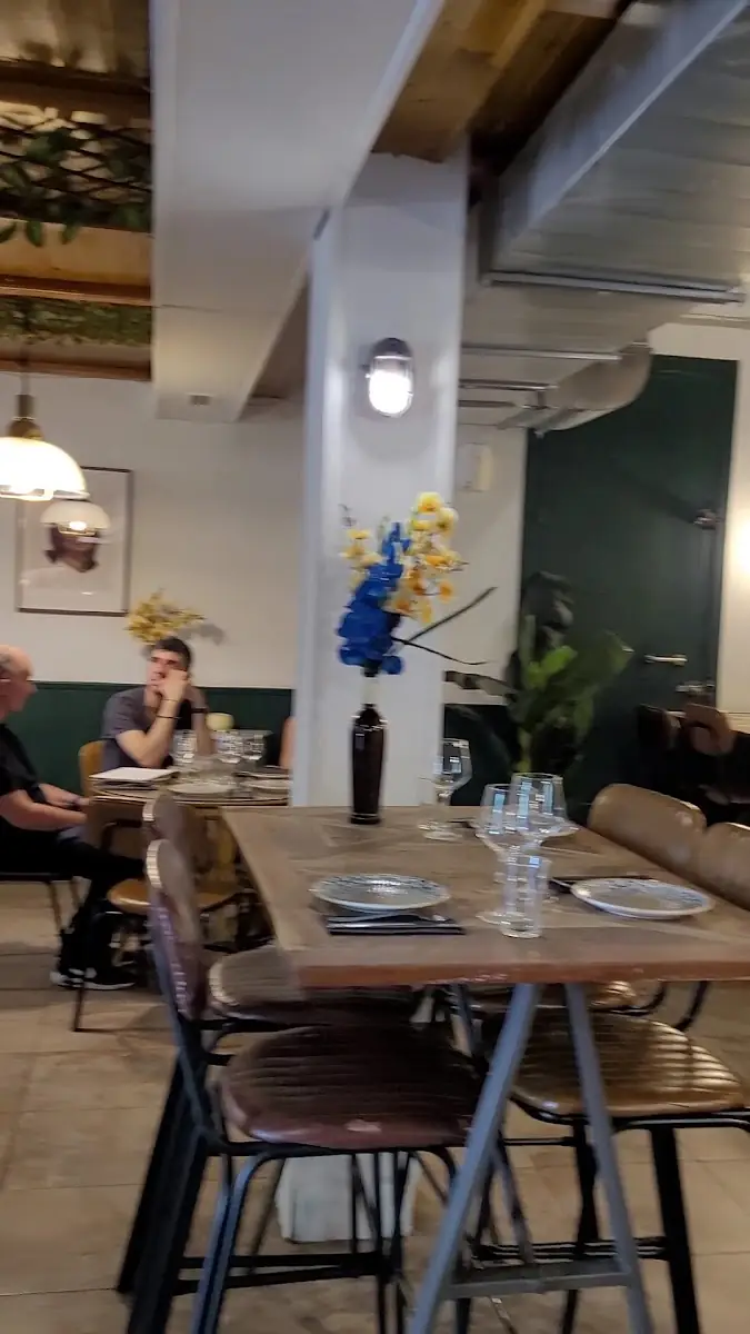 Dining room with set wooden tables, leather-backed chairs, a blue-and-yellow flower vase and a couple of diners in the background