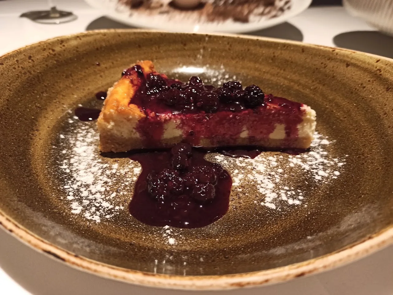 A slice of cheesecake topped with a berry compote and powdered sugar