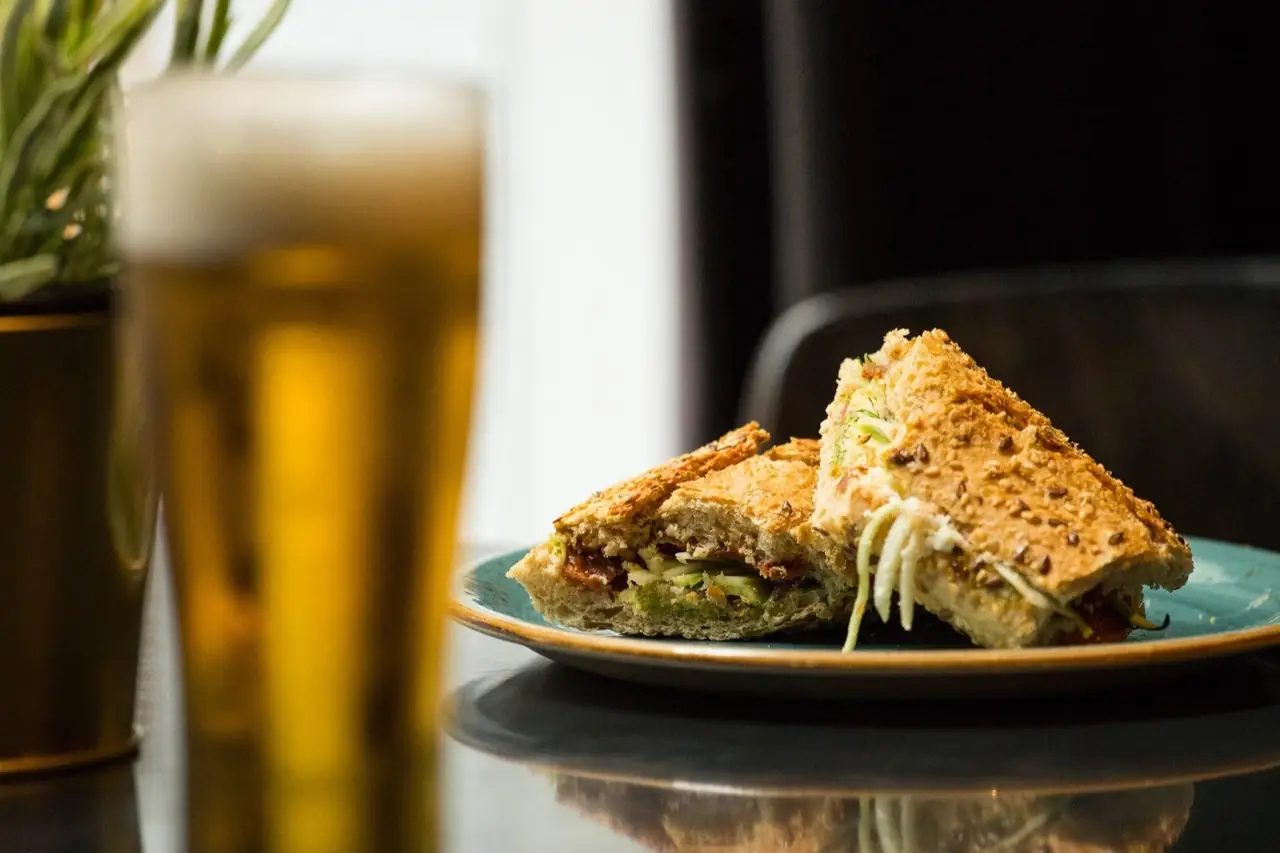Toasted seeded-bread sandwich cut in triangles on a teal plate beside a glass of beer