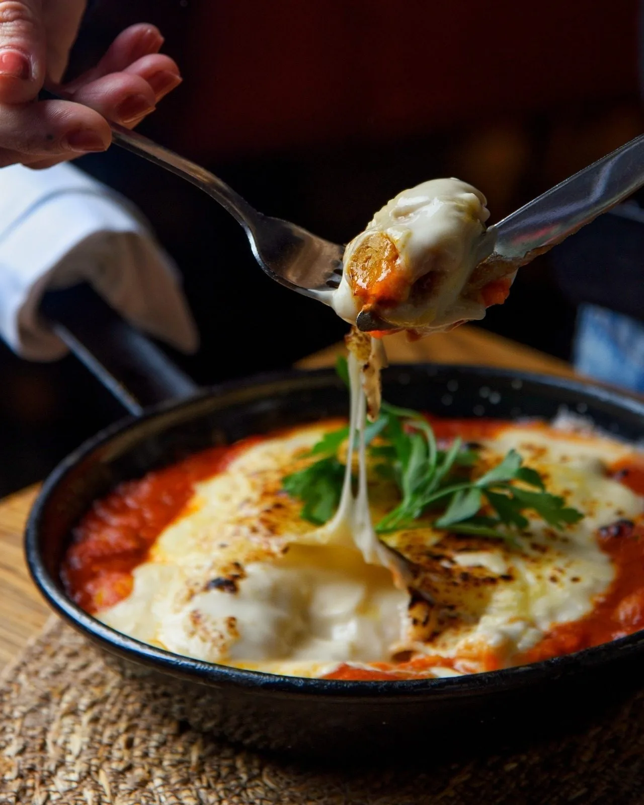 Baked eggs in tomato sauce with melted cheese in a black pan, being lifted with a fork