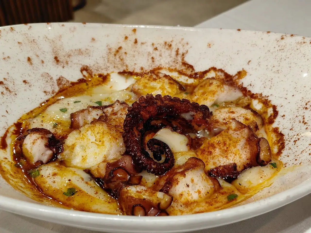 Grilled octopus slices over a paprika-dusted sauce on a white plate.