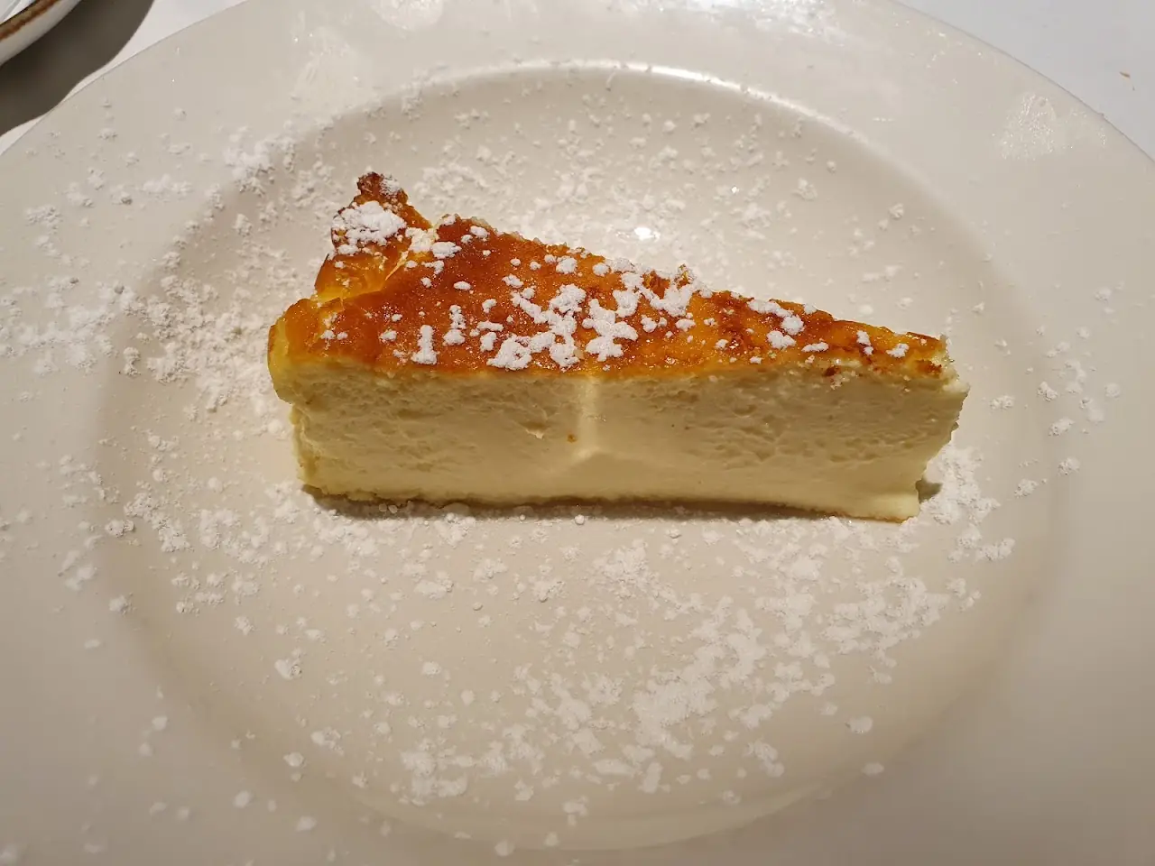A slice of cheesecake dusted with powdered sugar on a white plate.
