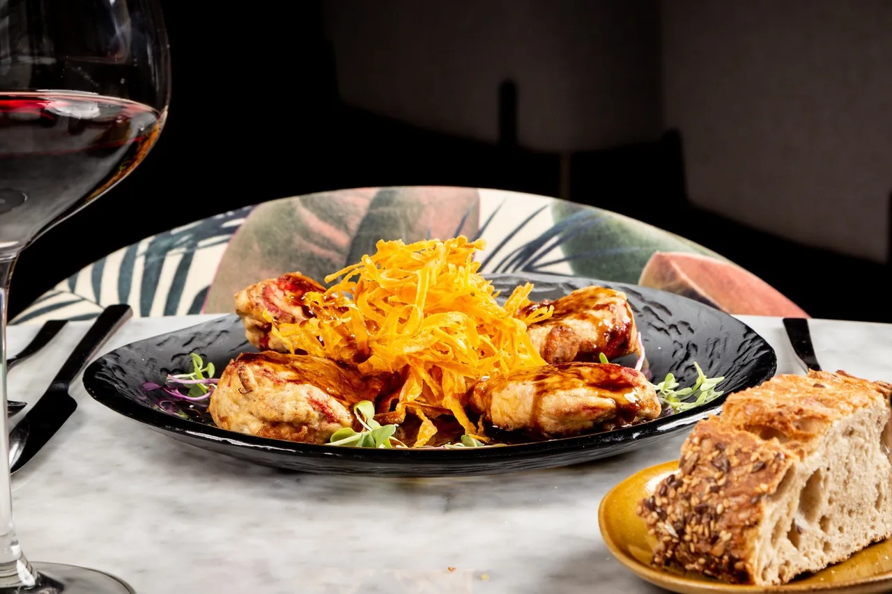 A plate of chicken pieces topped with carrot strands beside bread and a glass of wine