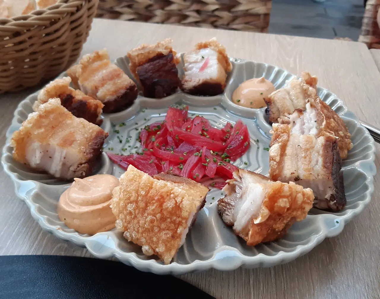 A plate of crispy pork belly bites with pickled red onion and two dipping sauces