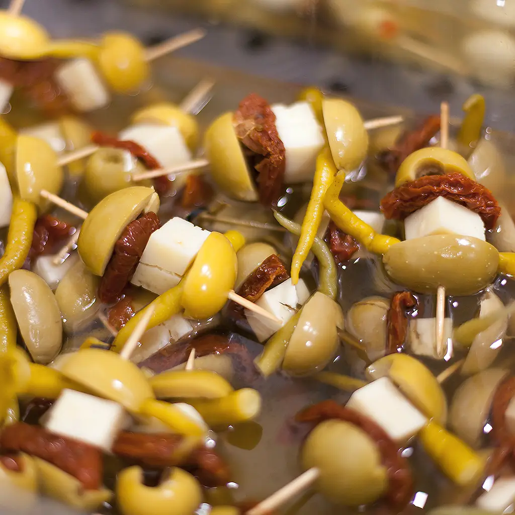 Close view of gilda pintxos on toothpicks with green olives, guindilla peppers, cheese cubes and sun-dried tomato in brine