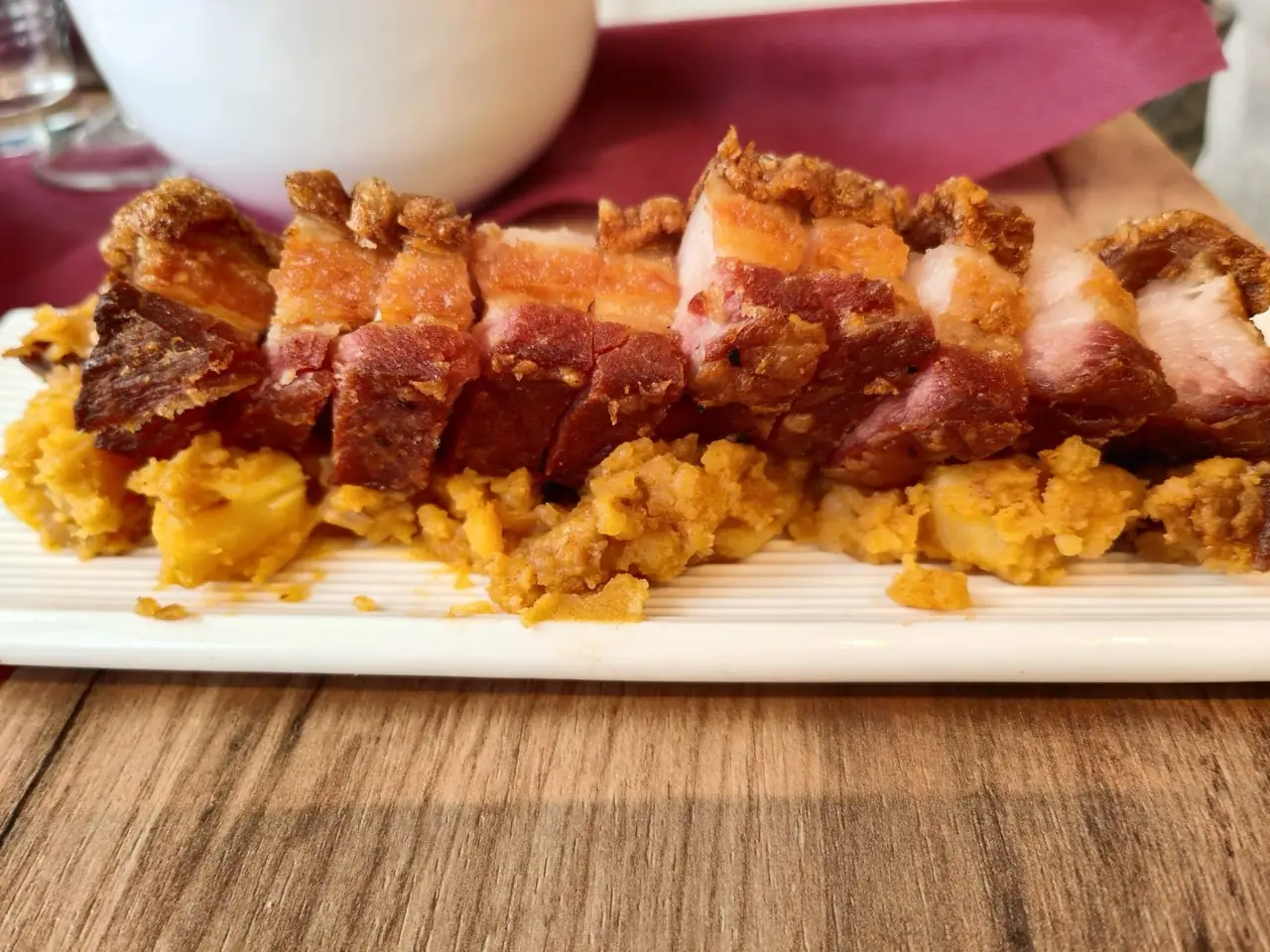 Sliced crispy-skinned roast pork belly laid over a bed of migas on a white plate