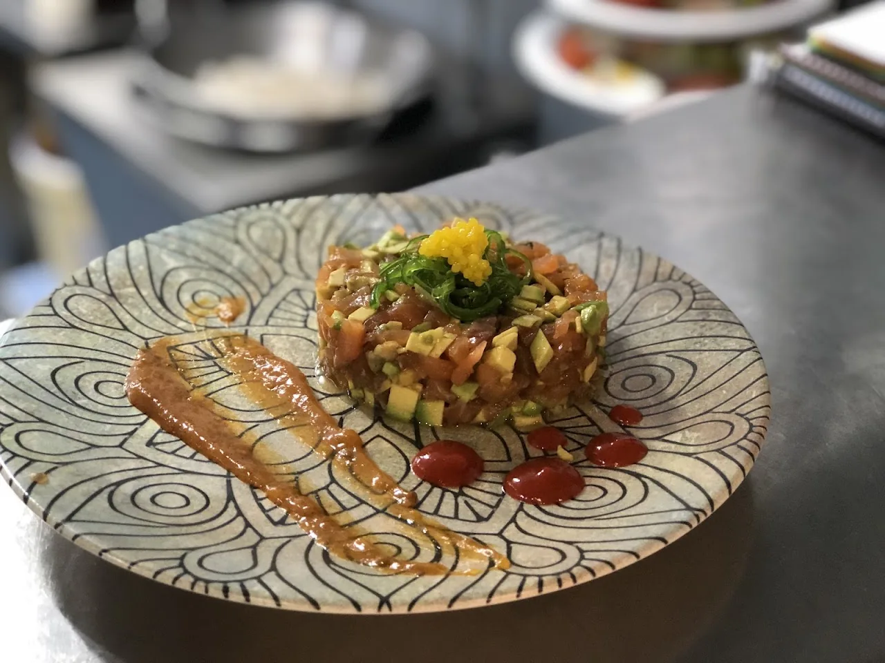 A tartare dish on a patterned plate with a swirl of orange sauce