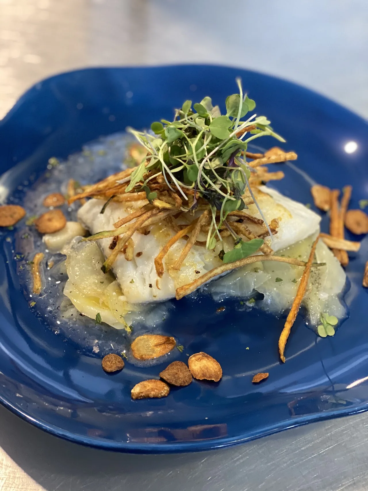 A piece of fish fillet garnished with herbs and almonds on a blue plate