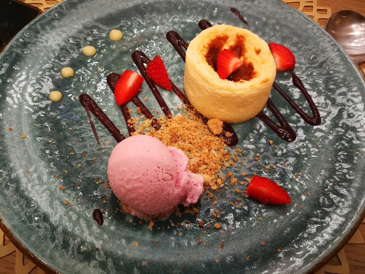 A dessert of sponge cake with strawberries, chocolate drizzle, and a scoop of pink sorbet
