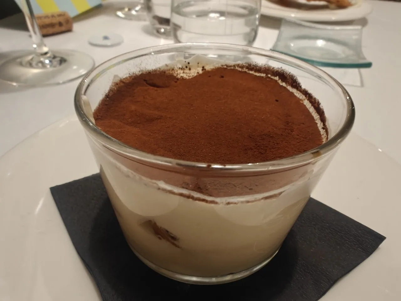 A glass dish of tiramisu dusted with cocoa