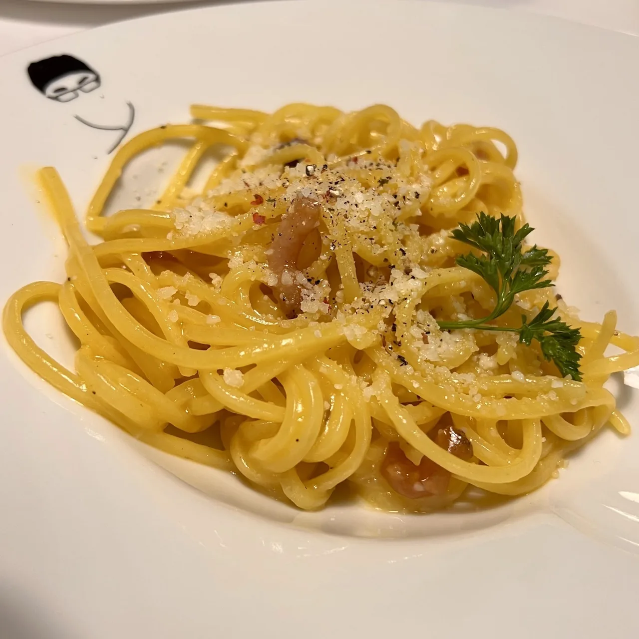 A white plate of spaghetti twirled into a nest with grated cheese and a sprig of parsley