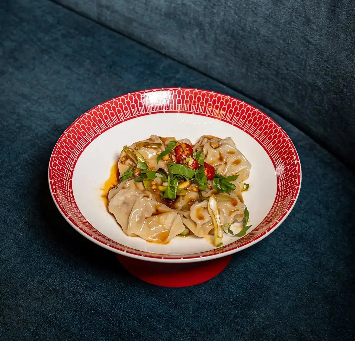 Dumplings in red chili oil in a red-patterned bowl on a dark blue surface