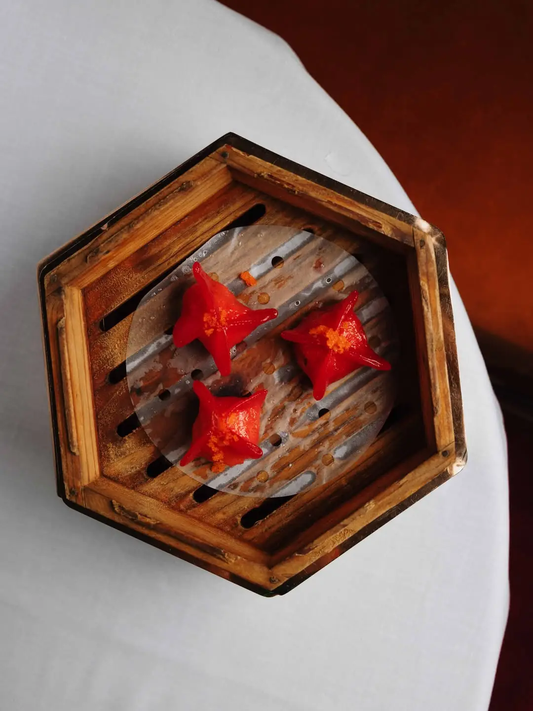Three star shaped red dumplings with orange roe garnish inside an open bamboo steamer basket