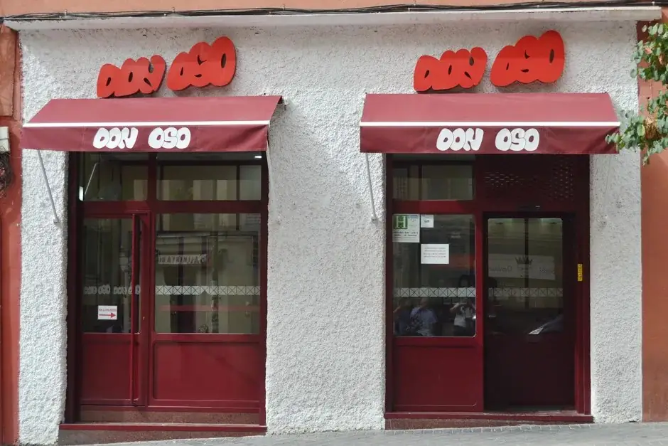 Storefront of Don Oso with two maroon awnings reading DON OSO and red 3D letter signage above red-framed glass doors on a white stucco facade