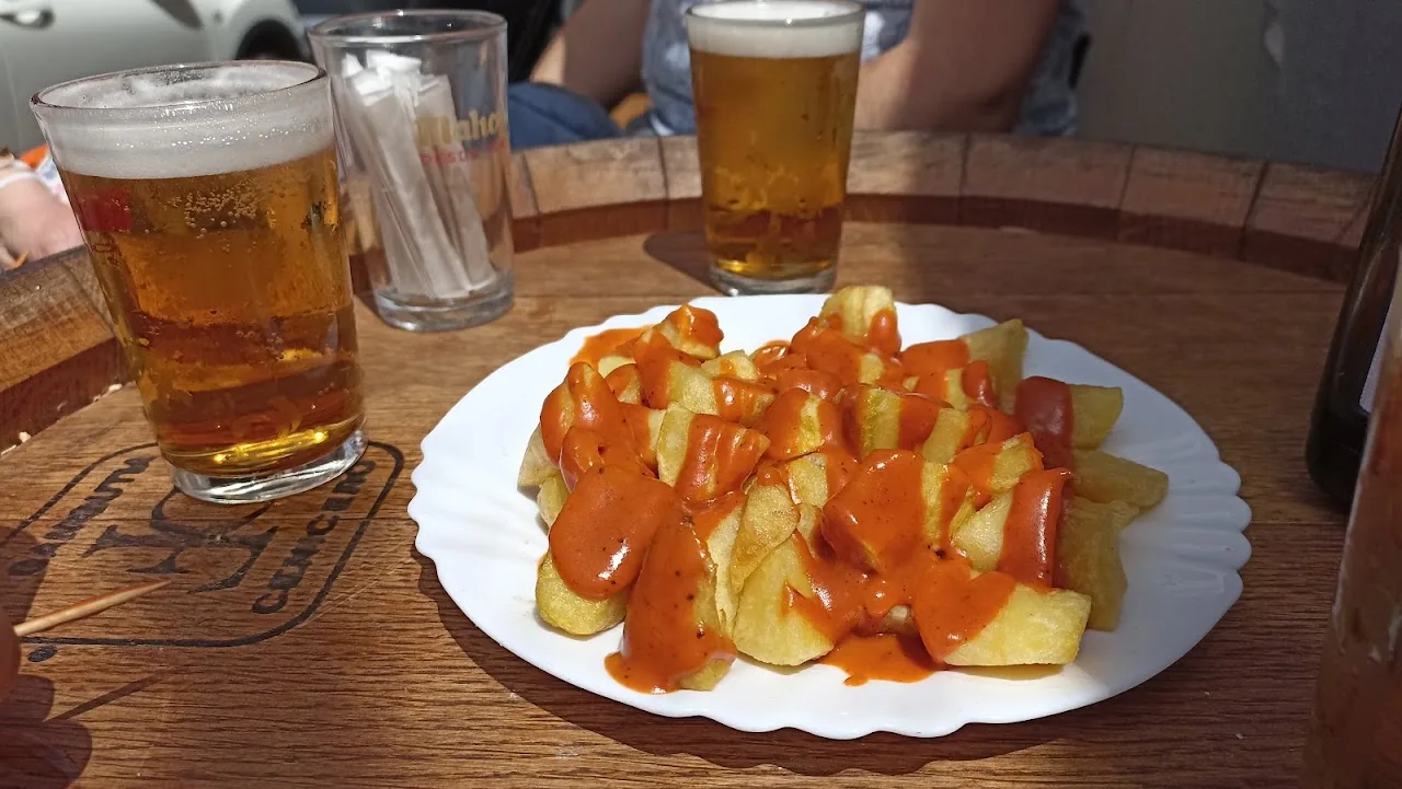 A plate of patatas bravas with fries and orange sauce, beers in the background