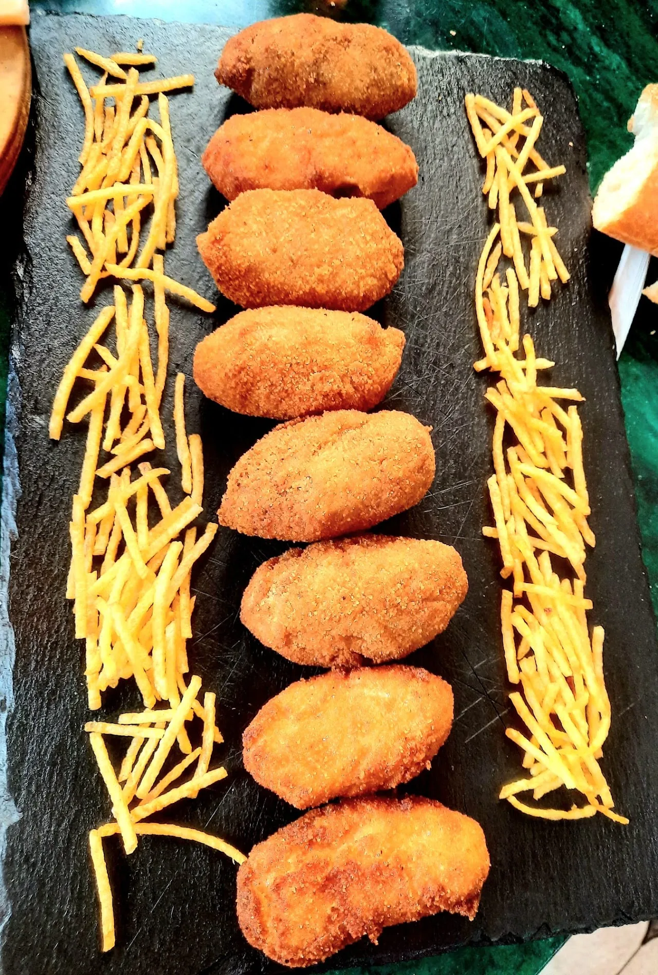 Breaded croquettes served with a side of shoestring fries on a slate board