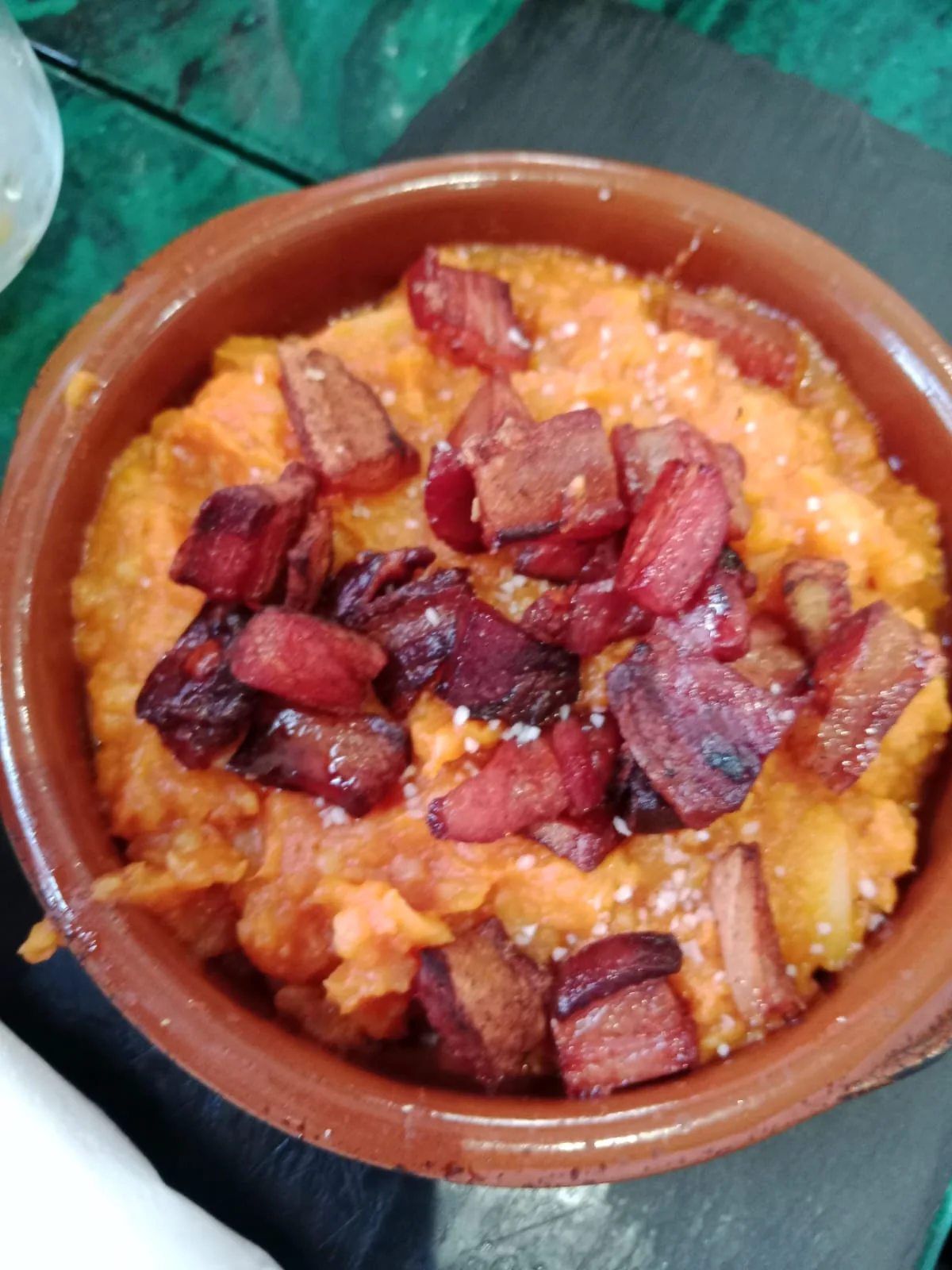 A bowl of fried potatoes topped with bacon bits and orange sauce