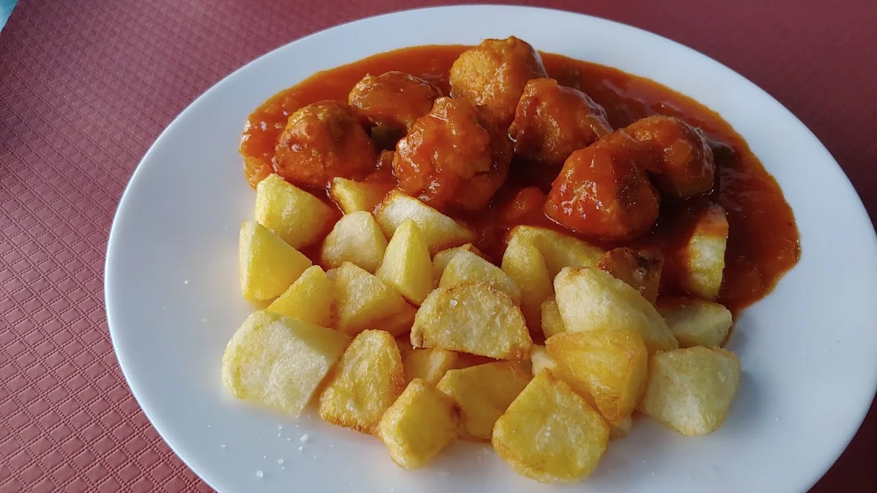 A plate of meatballs in tomato sauce with a side of patatas bravas