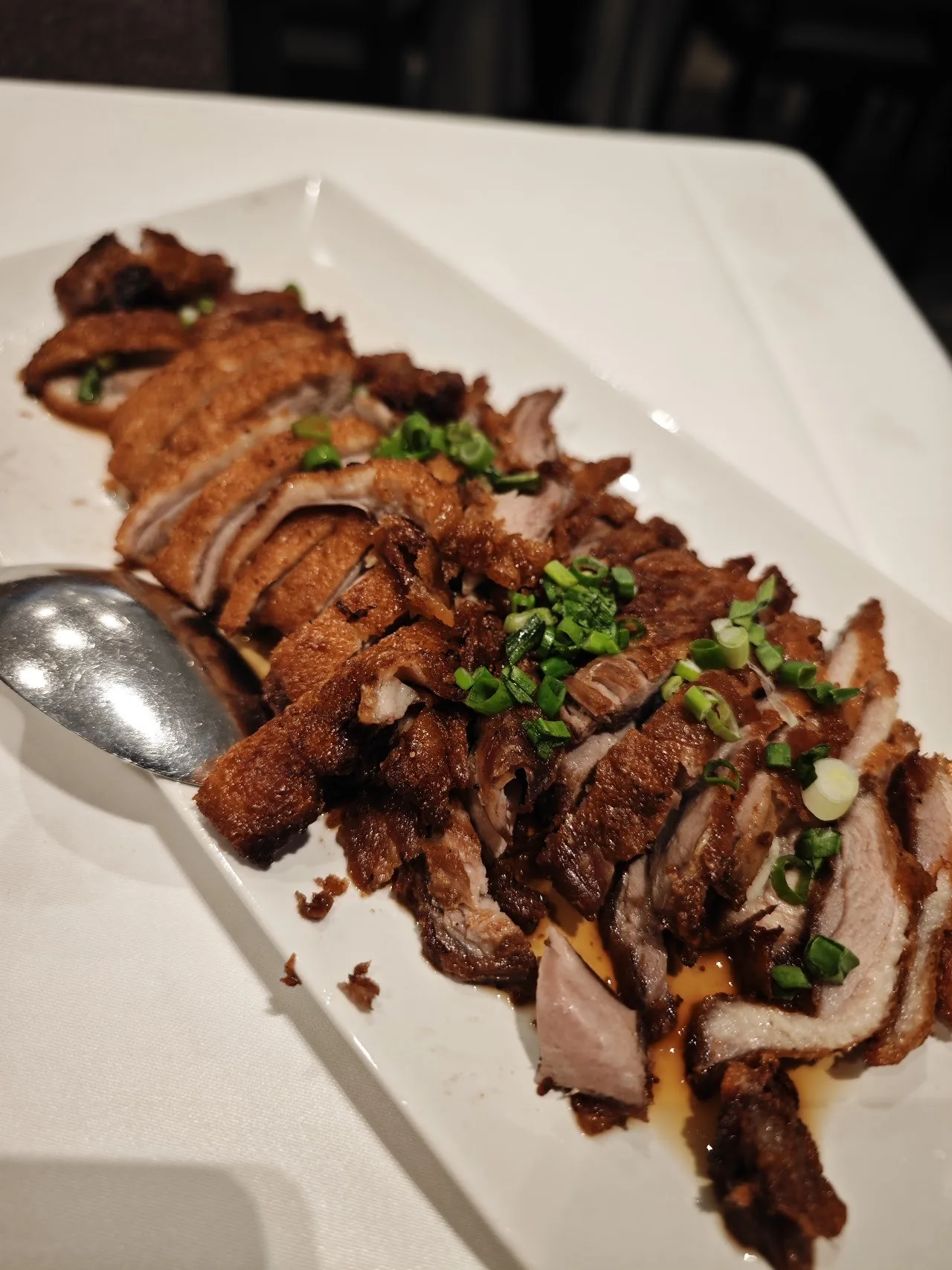 Sliced roast duck with chopped spring onion on a long white plate