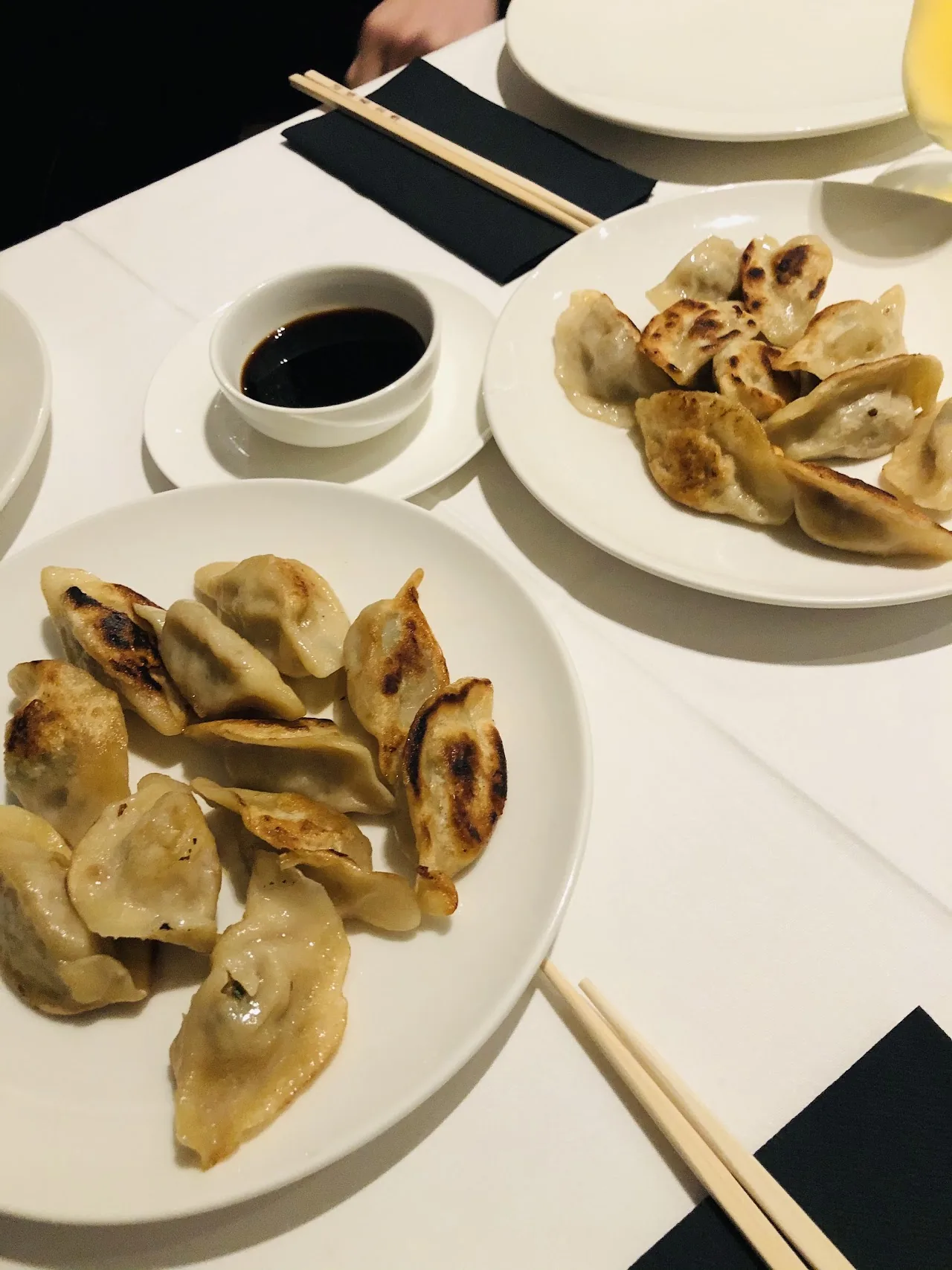 A plate of pan-fried dumplings with a small bowl of soy sauce