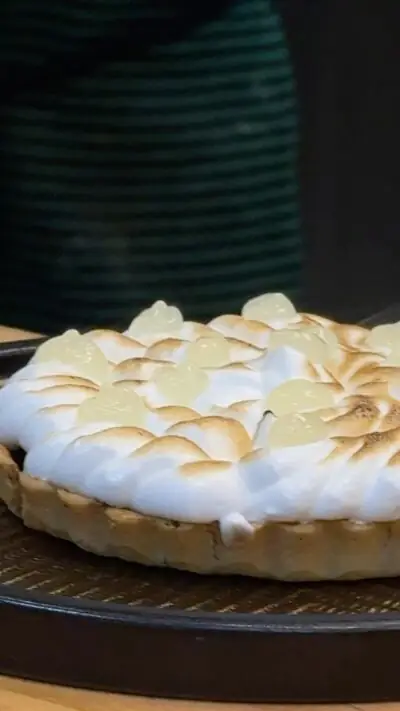 Torched meringue-topped tart with pastry crust on a dark plate over a woven mat