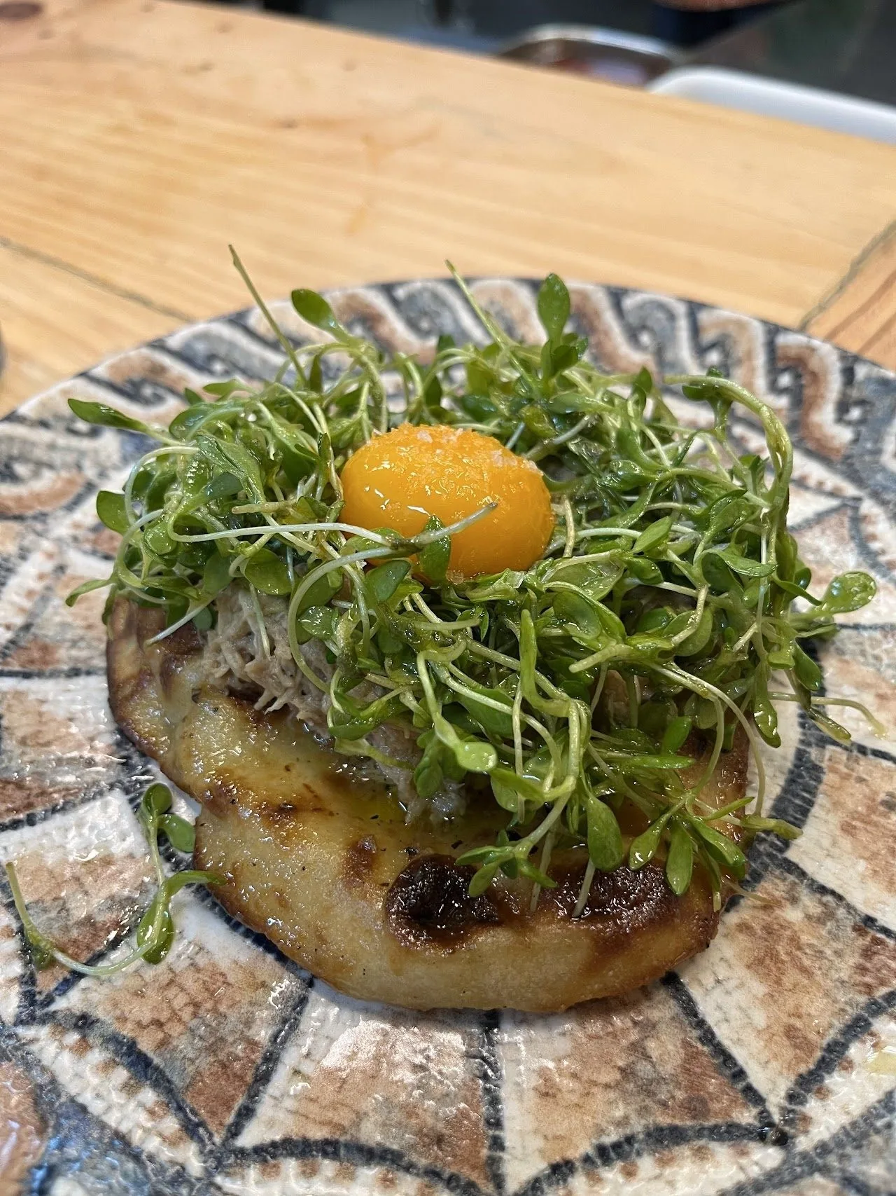 A patterned plate holding a round dish topped with sprouts and an egg yolk