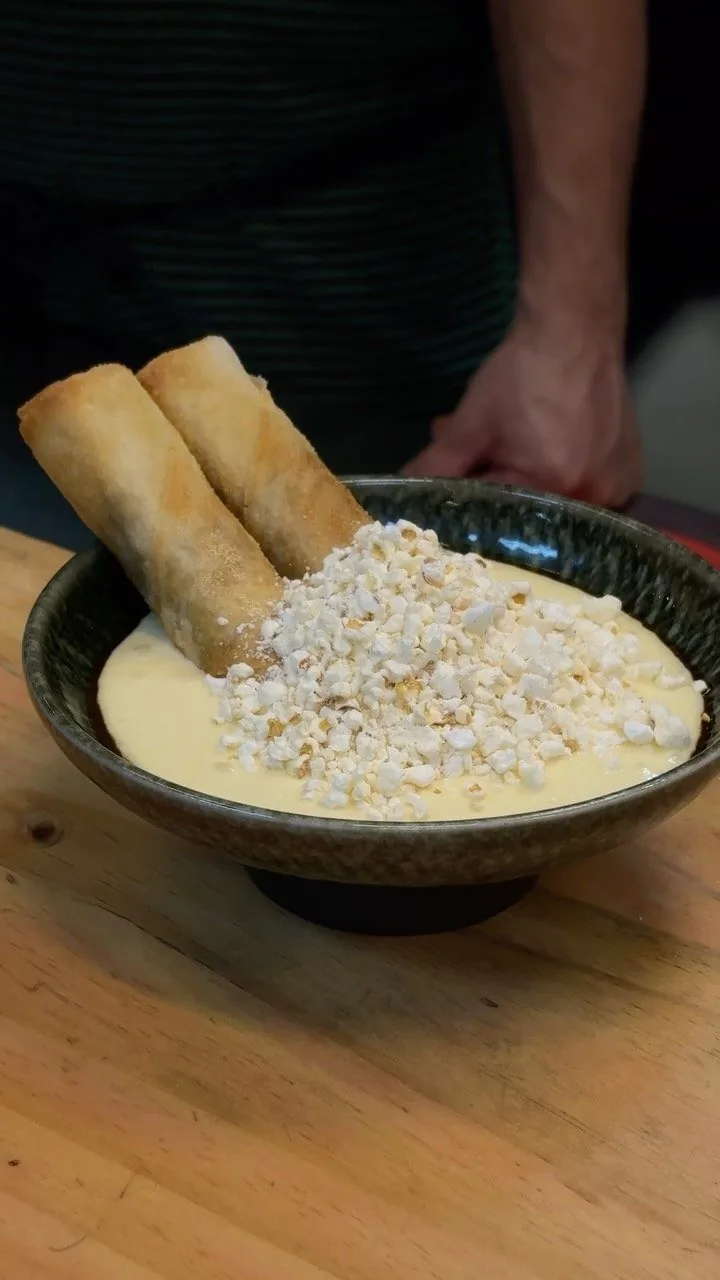 Two crisp rolls standing in a dark bowl of creamy sauce with a crumbled topping