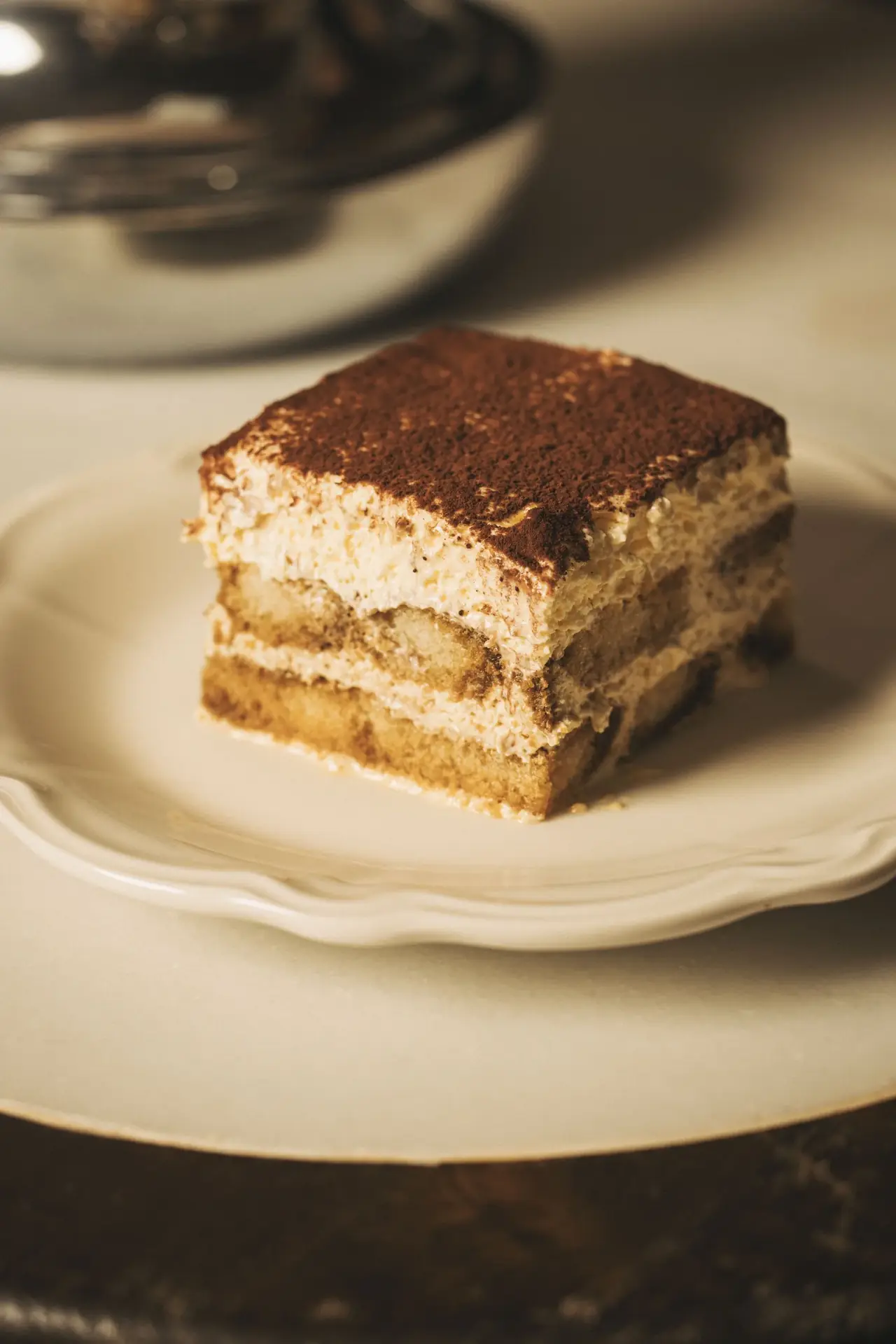 A slice of tiramisu dusted with cocoa powder on a white plate, Doppietta