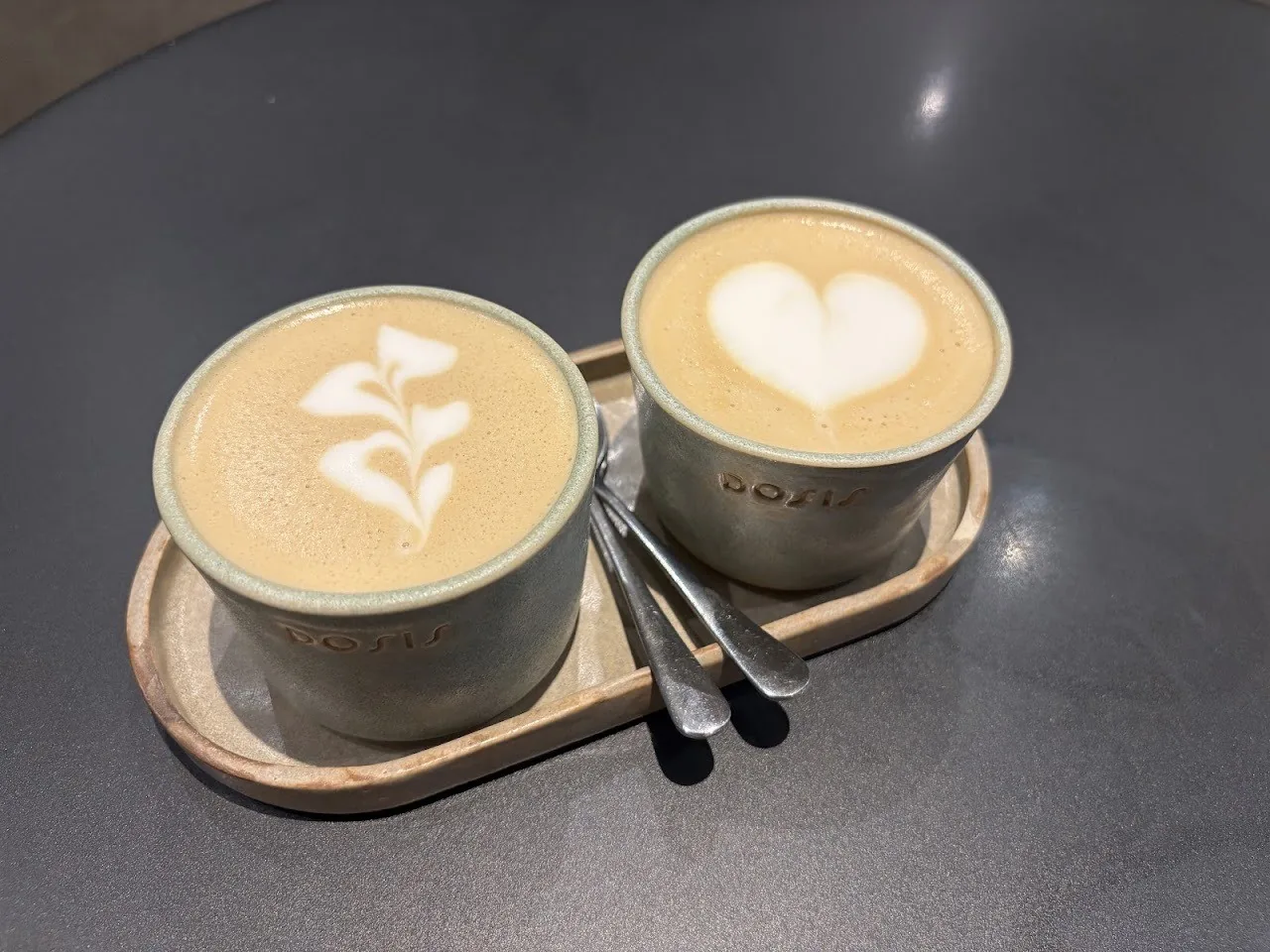 Two cups of latte with heart and leaf art on small grey trays