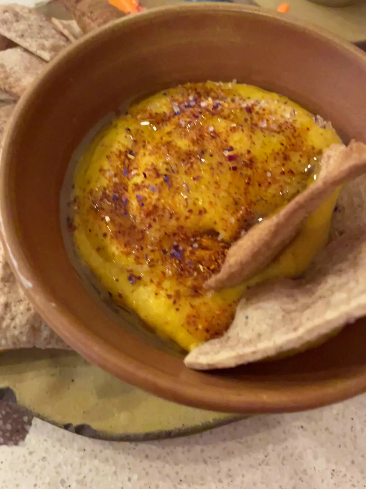 A bowl of a yellow dip or spread with a piece of flatbread