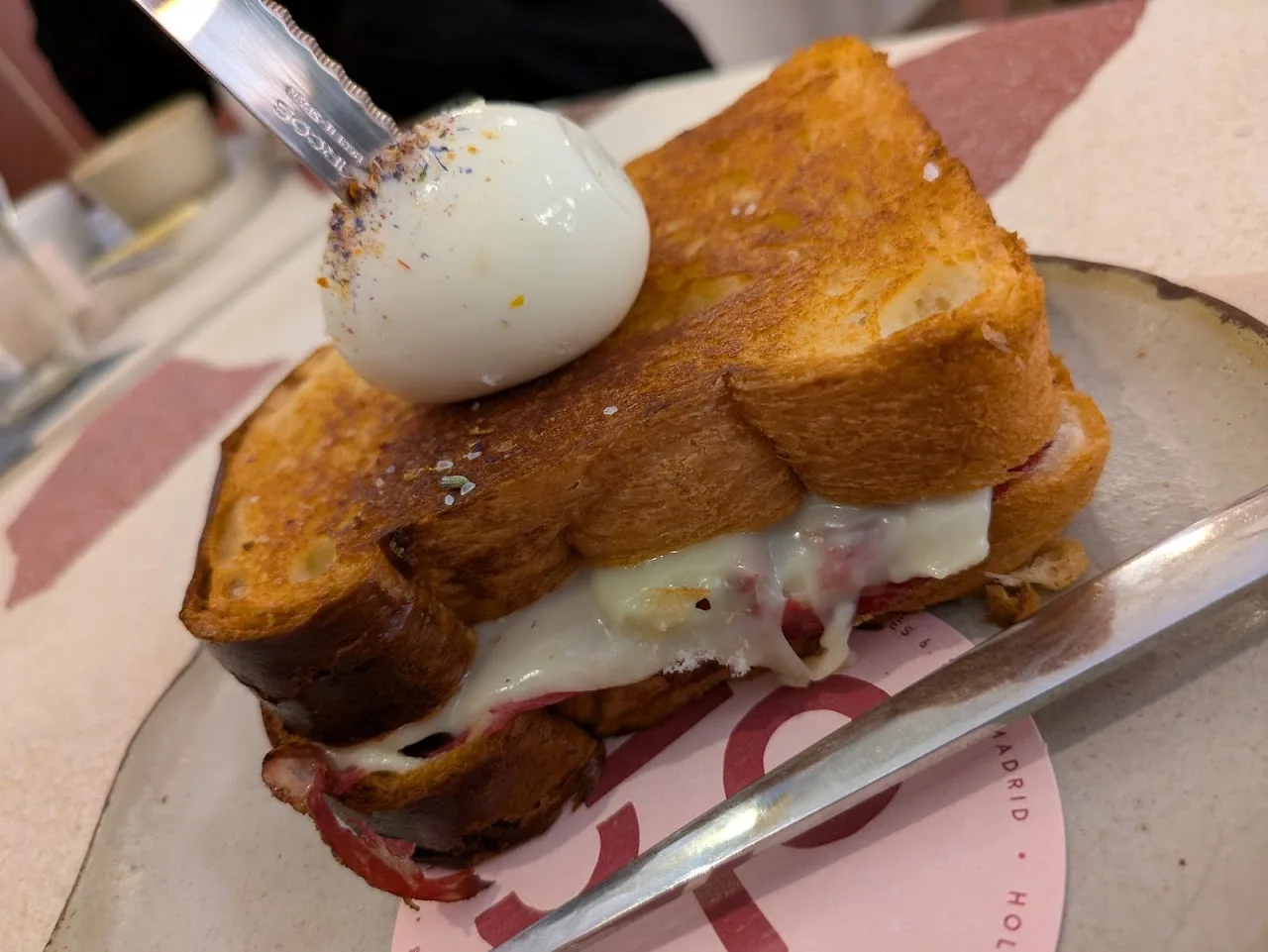 A grilled sandwich with melted cheese topped with a soft-boiled egg