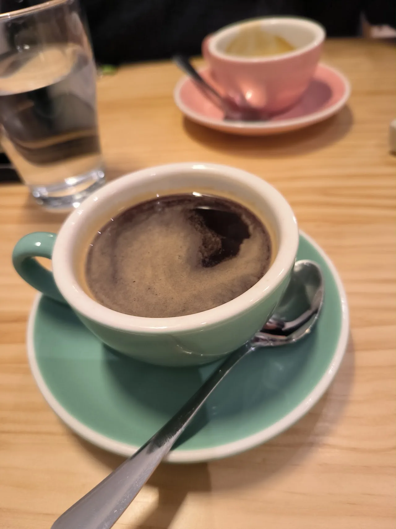 A cup of black coffee on a saucer with a spoon