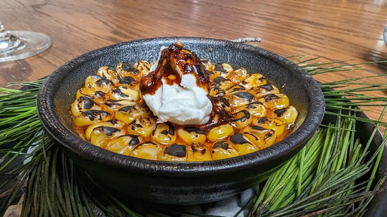 Charred corn kernels with a dollop of cream and dark sauce in a black bowl