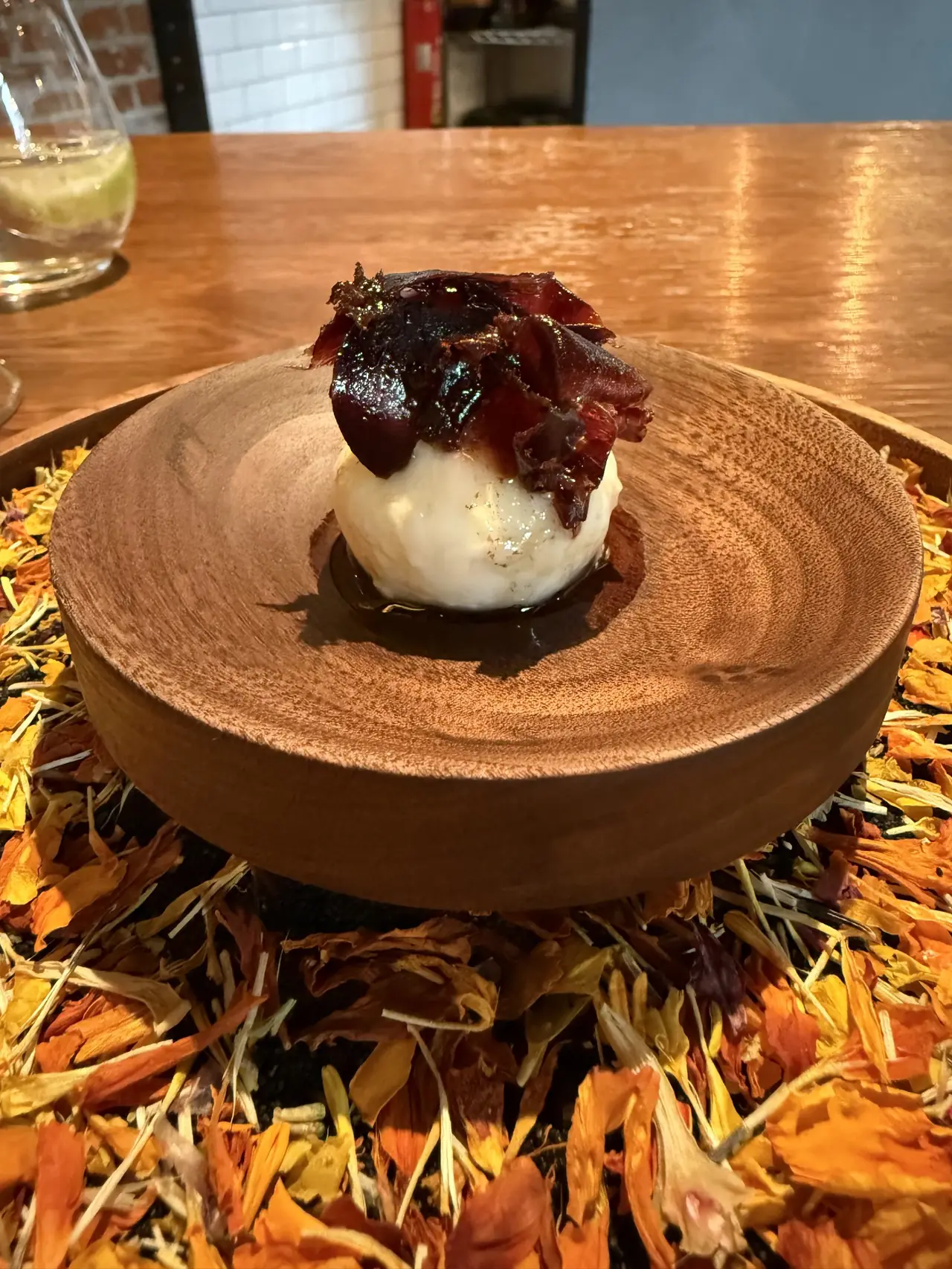 Round white cheese or ice cream ball topped with dark cured meat on a wooden plate