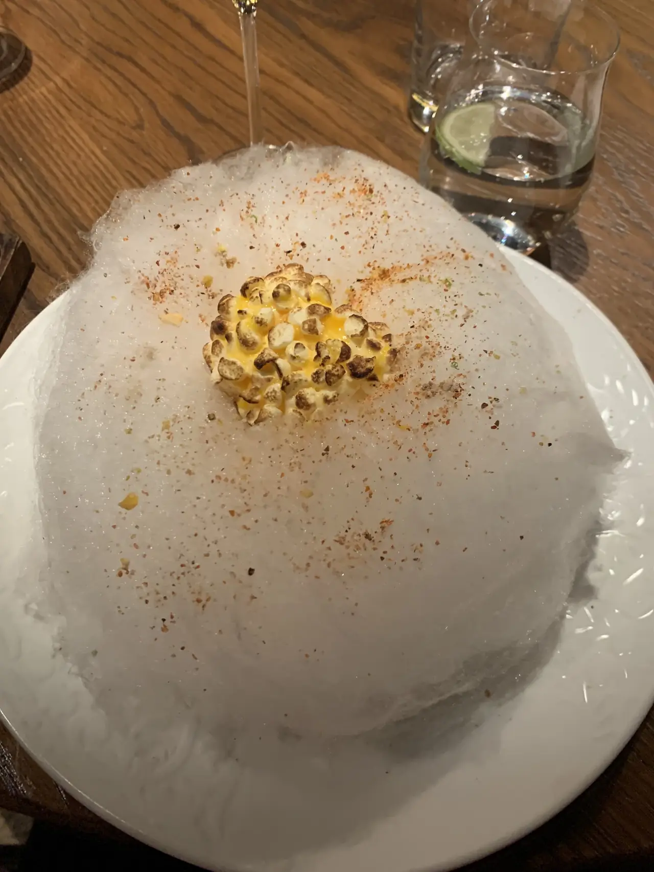 Popcorn-like corn dish on a bed of cotton candy with spice dusting on a white plate