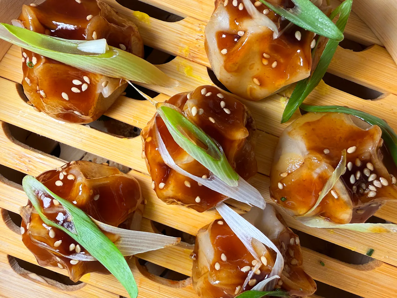 Glazed bao buns garnished with scallion, arranged on a board