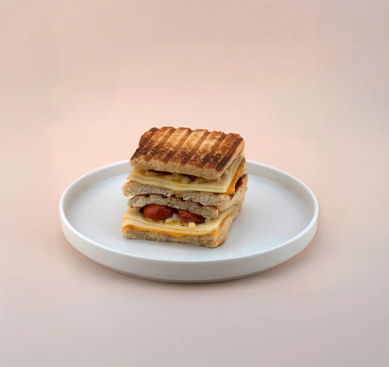 A grilled sandwich cut in half and stacked on a white plate.