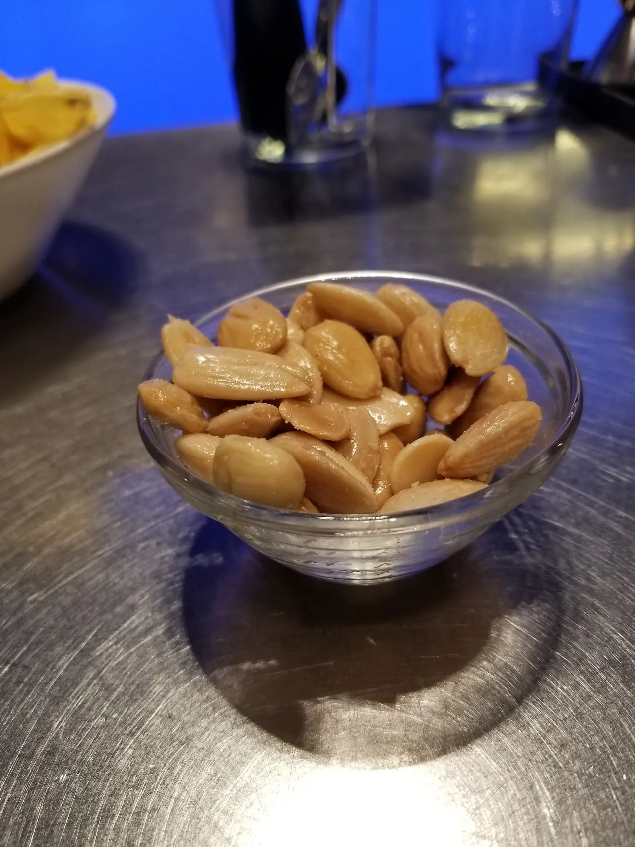 A glass bowl of almonds on a bar counter