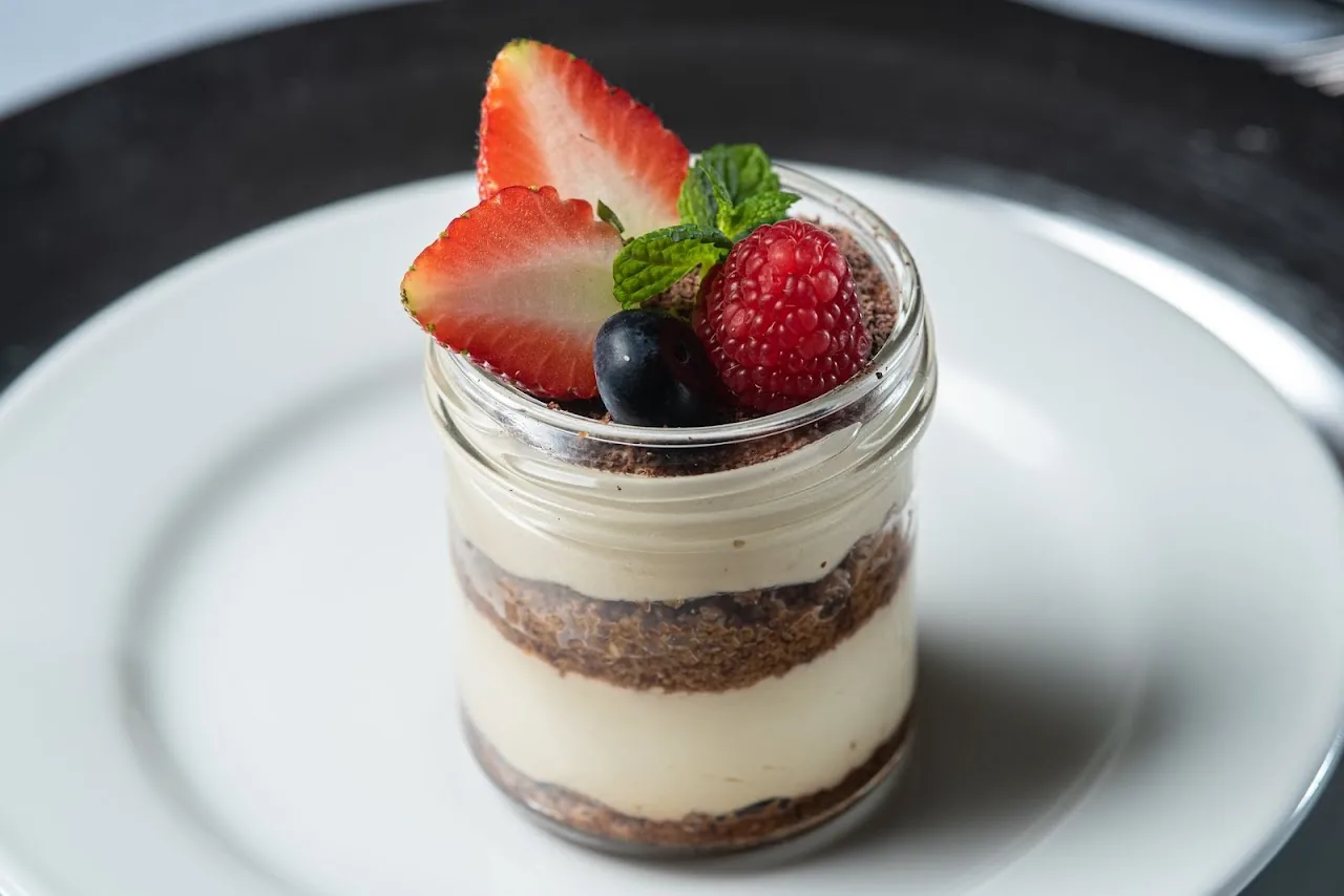 A layered dessert in a glass jar topped with strawberries and blueberries