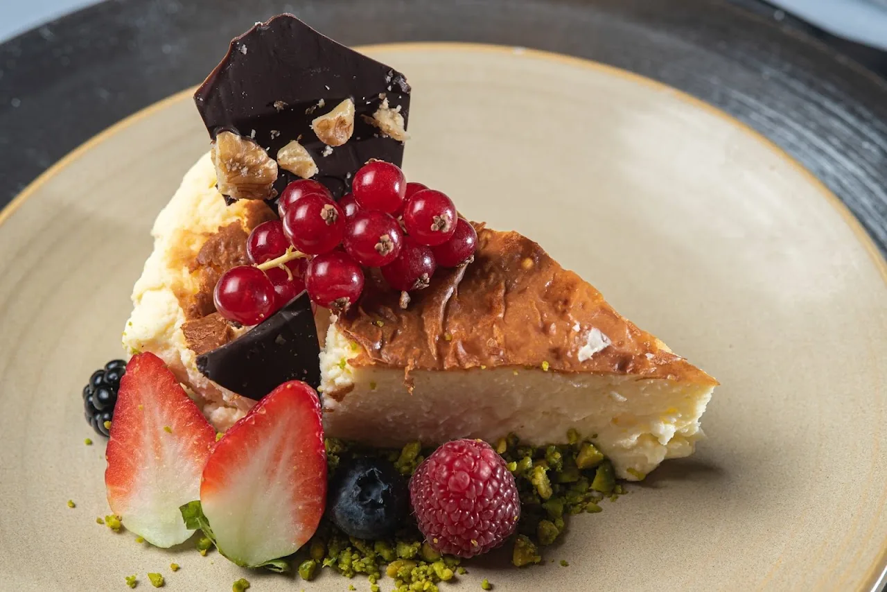 A slice of cheesecake garnished with berries and a chocolate shard