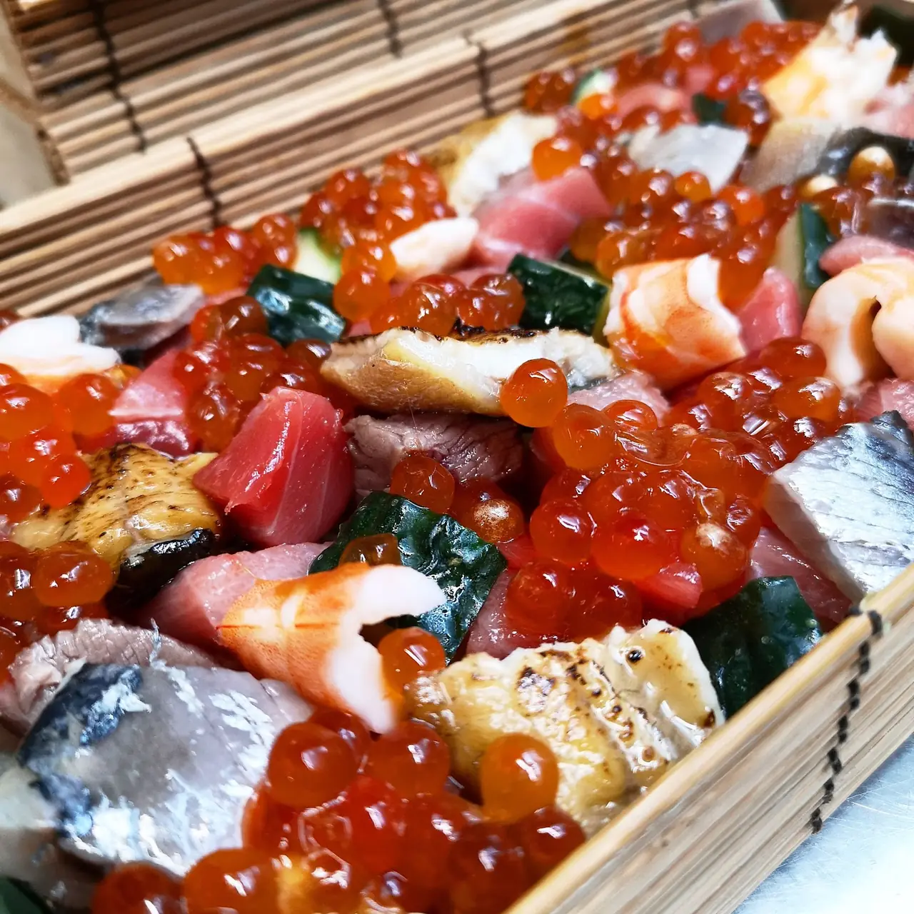 Assorted sashimi and seared fish topped with salmon roe in a bamboo box