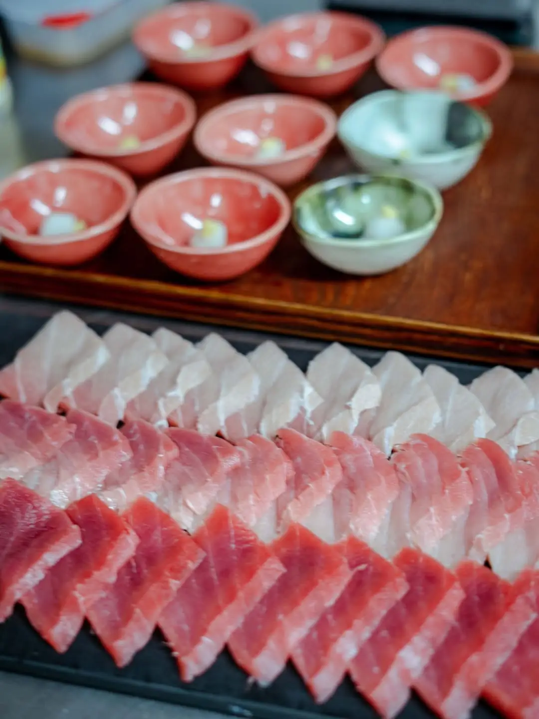 Rows of sliced tuna sashimi with small bowls of wasabi and pickled ginger