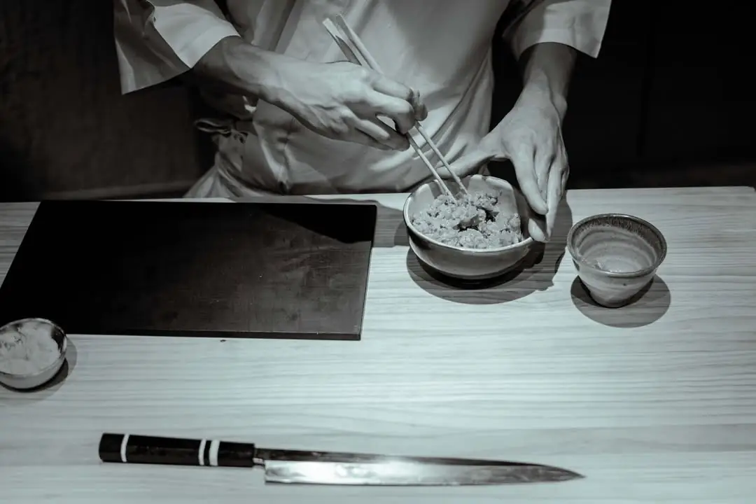 Chef mixing rice with chopsticks in a bowl beside a knife on the counter