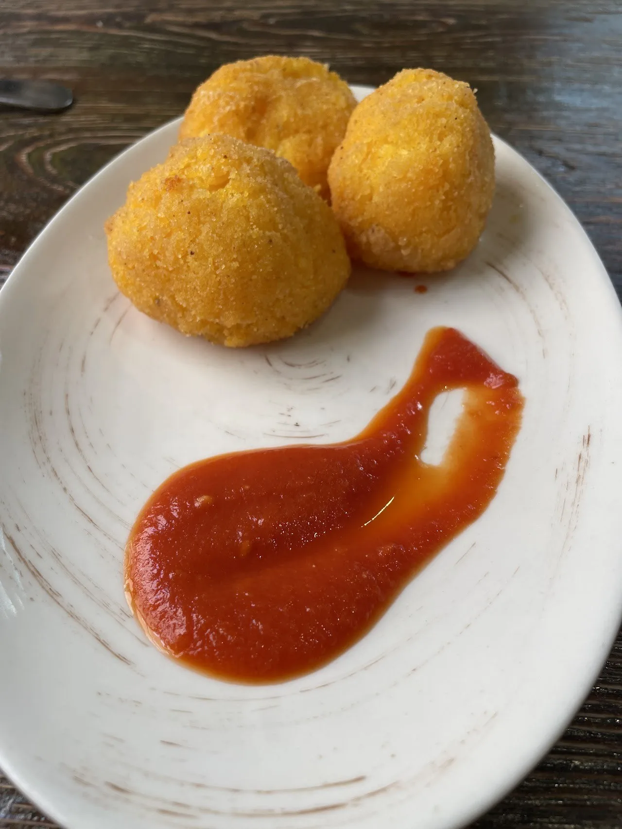 Golden fried rice balls on a white plate beside a swirl of red sauce