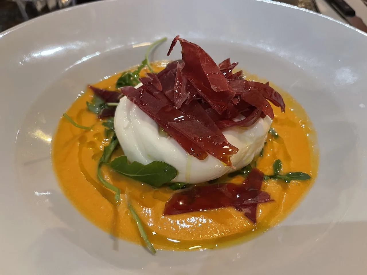 Burrata cheese topped with prosciutto and a swirl of sauce