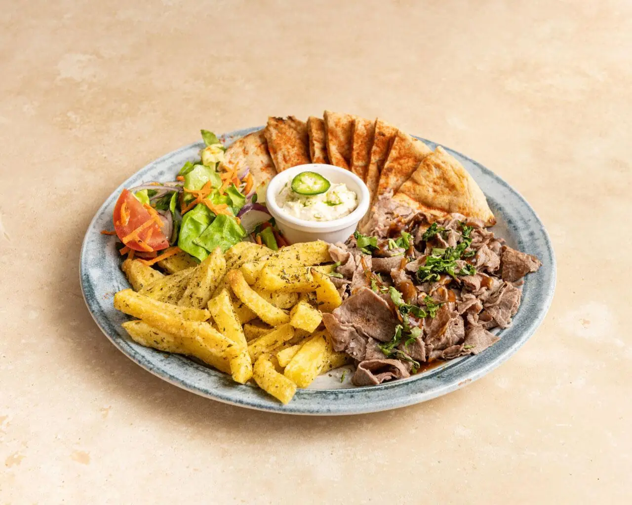 Gyros platter with sliced roast meat, seasoned fries, pita triangles, a salad and a cup of tzatziki on a blue-rimmed plate