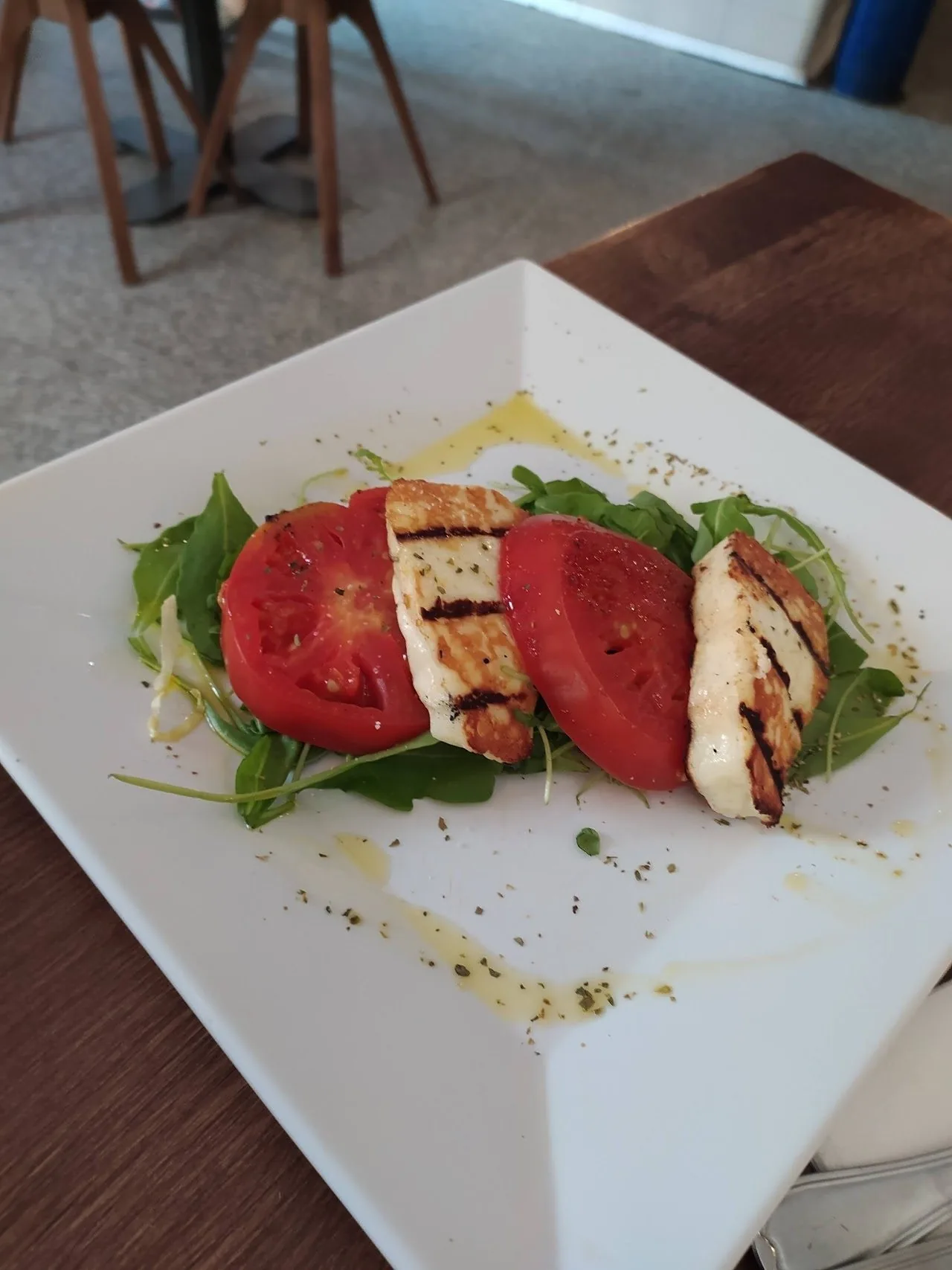 Slices of grilled cheese and tomato on leaves on a square white plate